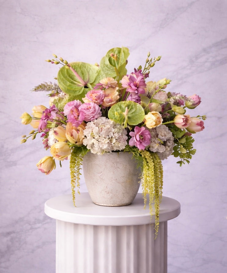 Floral arrangement in a pot on a white pedestal against a light gray background