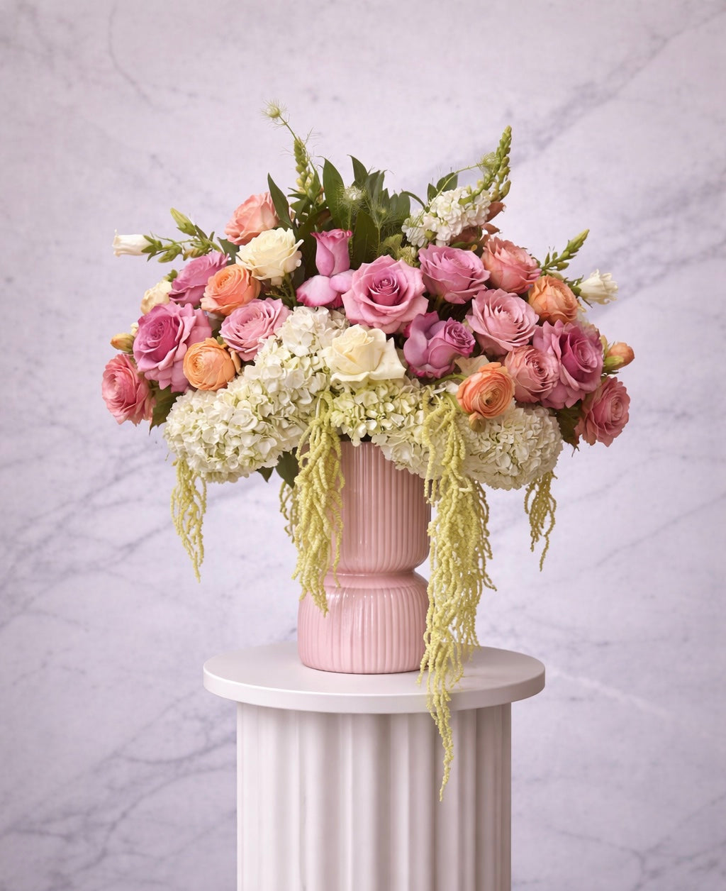 Floral arrangement in a pink vase on a white pedestal against a light gray background